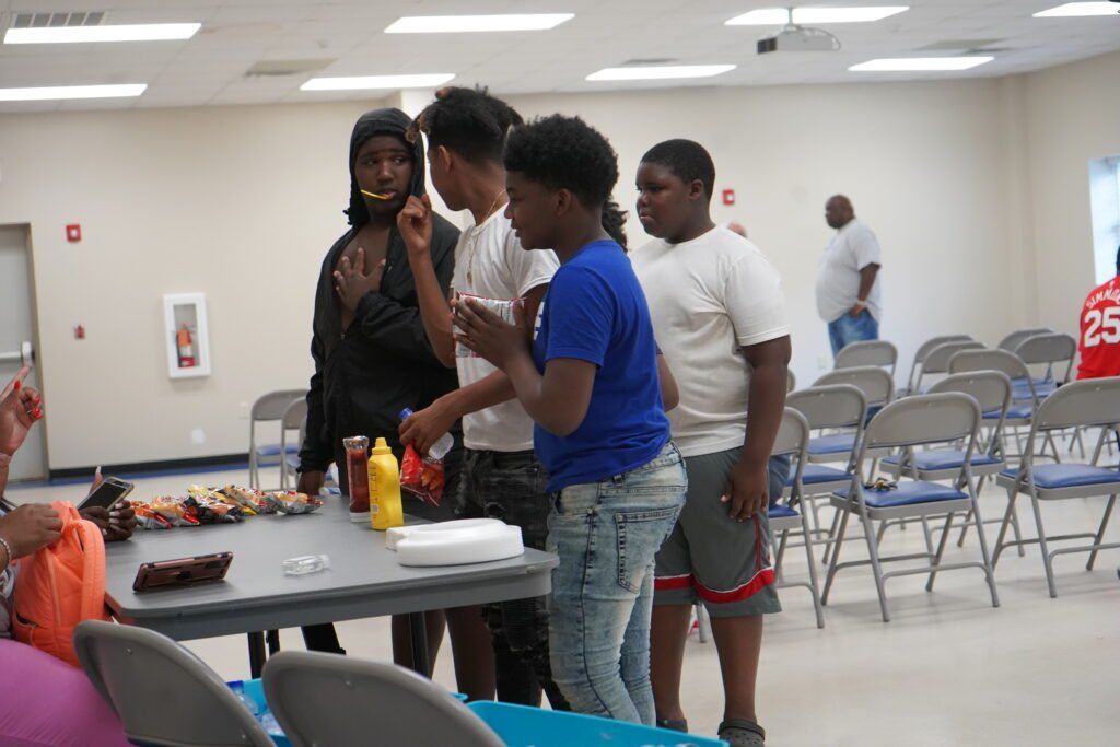 A group of people standing around a table with a bottle of ketchup on it