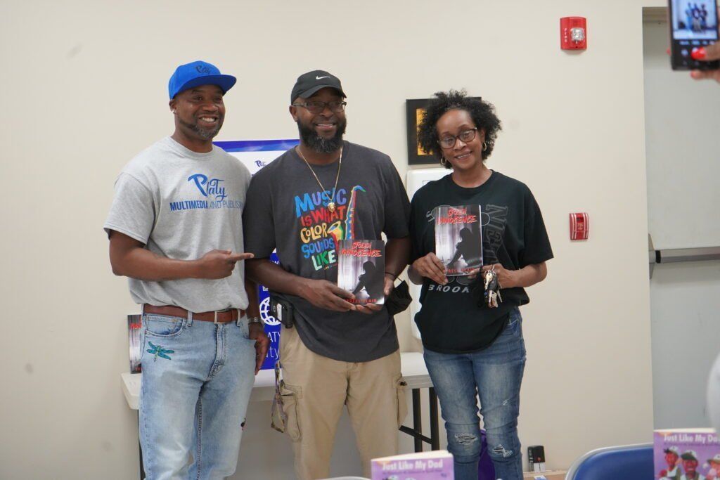 Three people are standing next to each other in a room holding books.