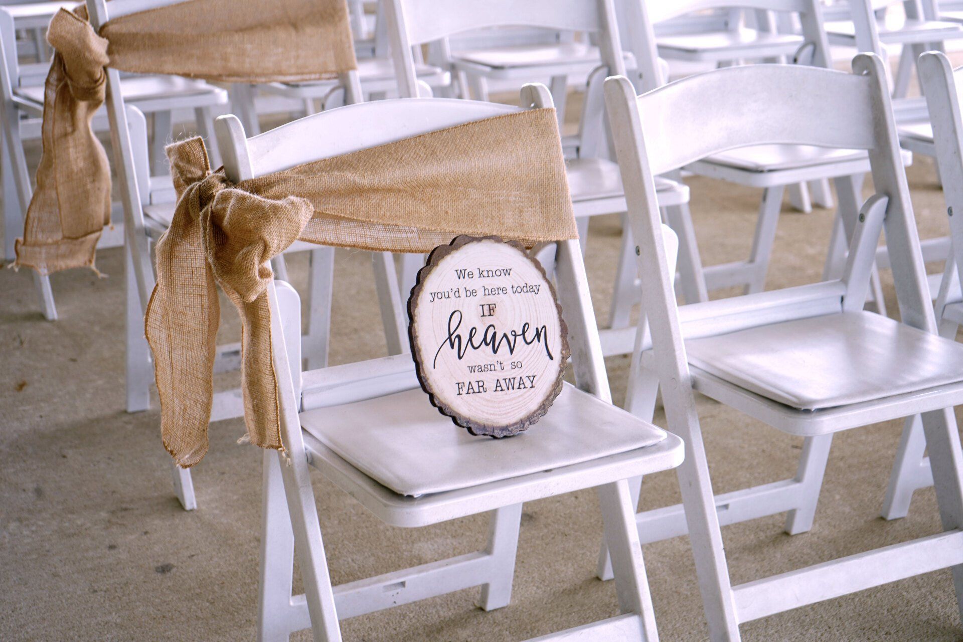 A wooden sign is sitting on the back of a white folding chair.