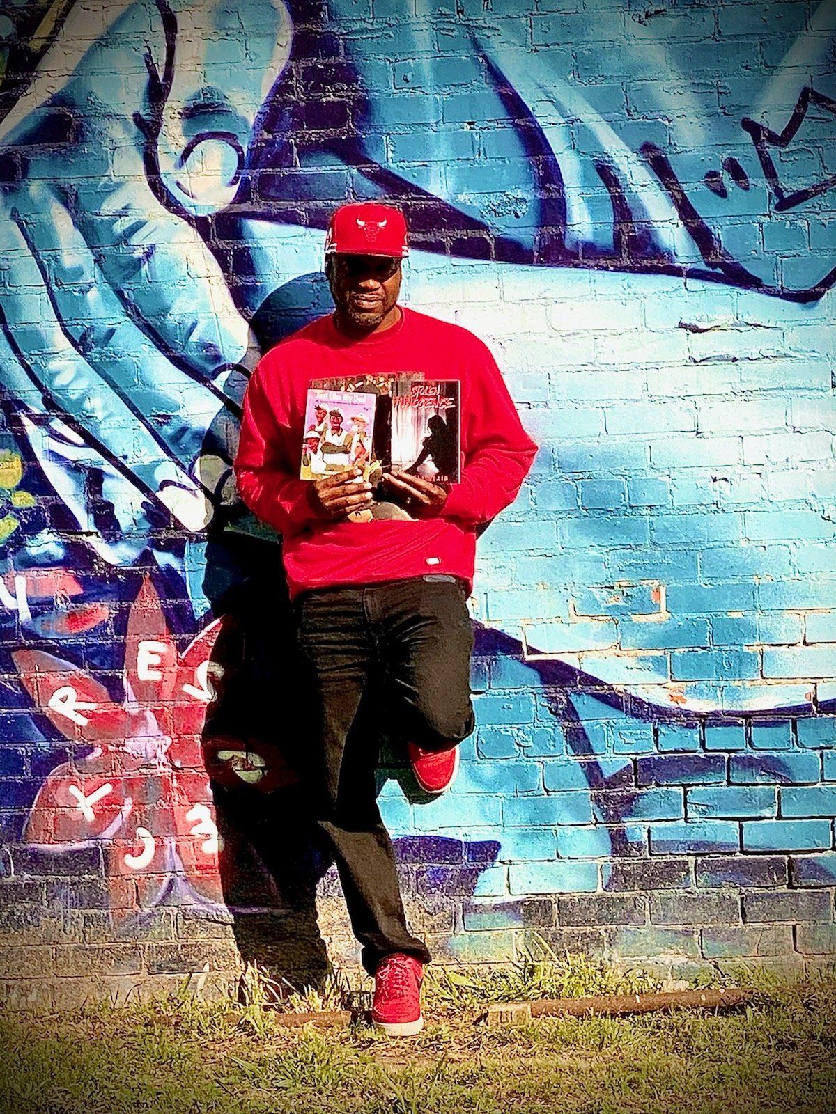 A man is standing in front of a brick wall holding a book.