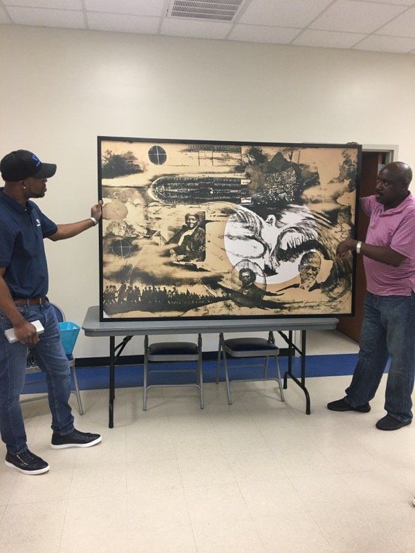 Two men are standing next to a large painting on a table