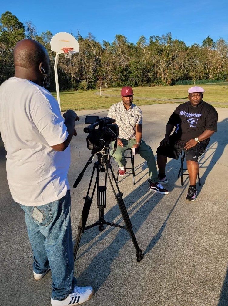 A man is standing in front of a camera talking to two men