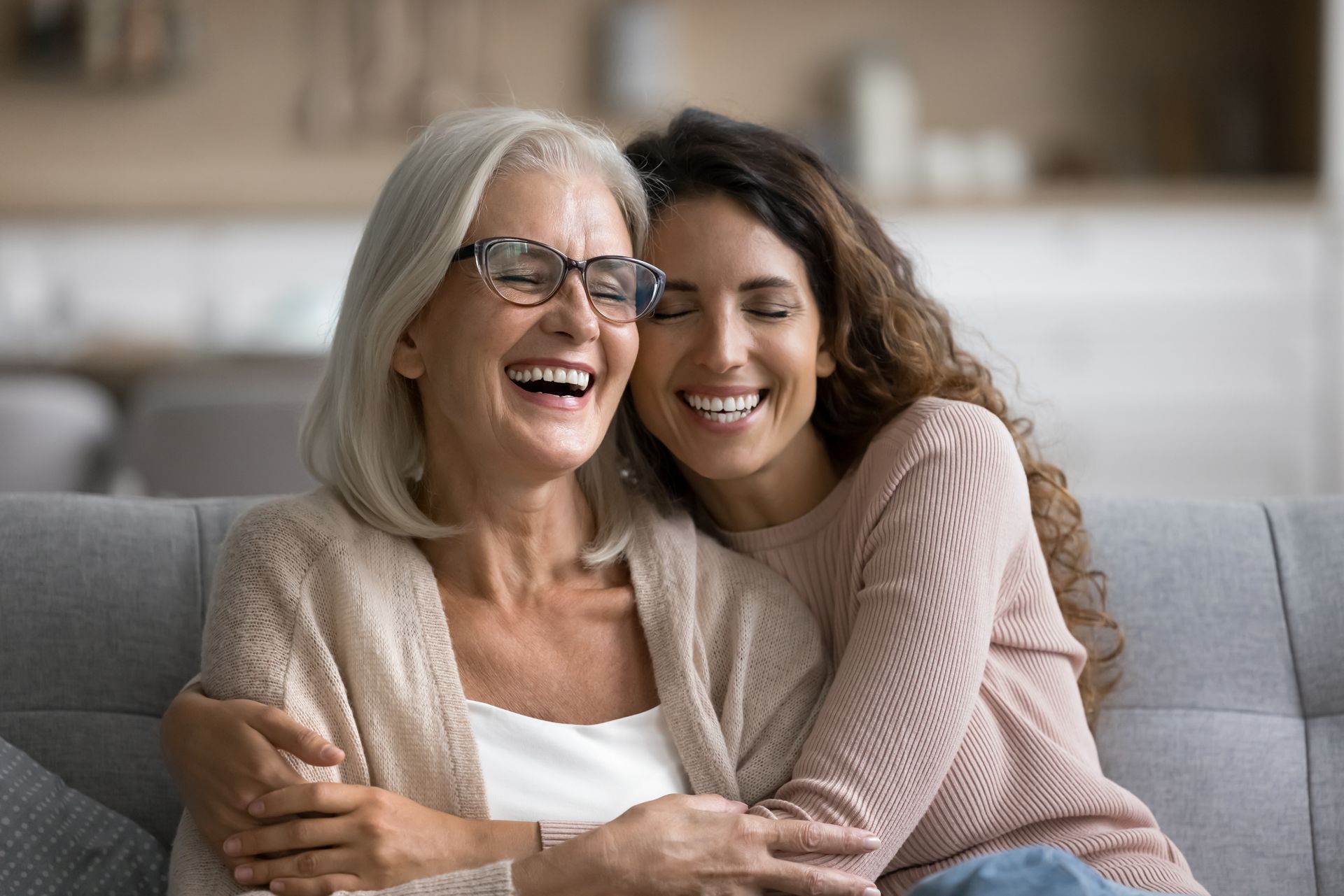 Mother and daughter laughing, embracing on a couch