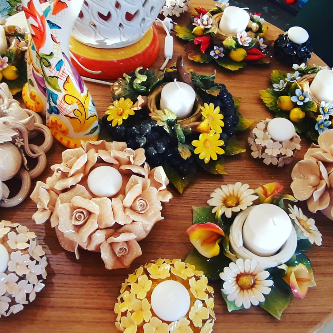 Portacandele con motivi floreali in ceramica su un tavolo di legno, vari colori e dimensioni.