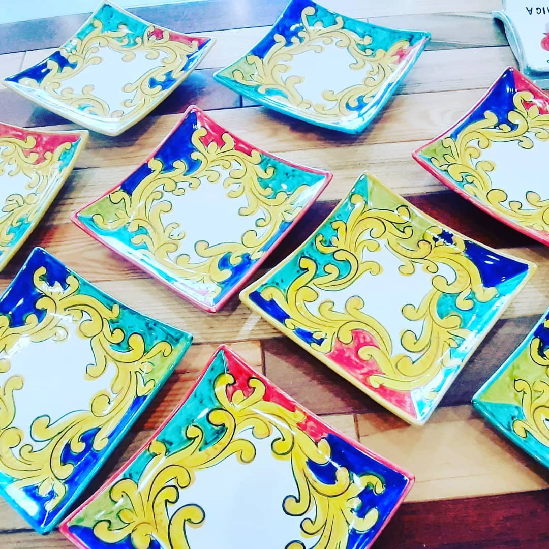 Piatti quadrati colorati con vortici dorati e bordi dipinti, disposti su una superficie di legno.