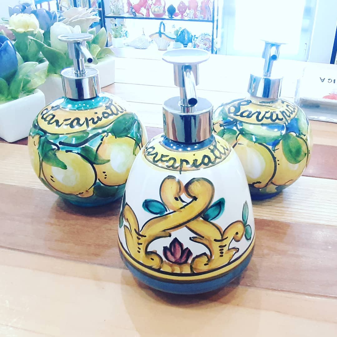 Tre dispenser decorativi in ceramica con motivi a forma di limoni su un tavolo di legno.