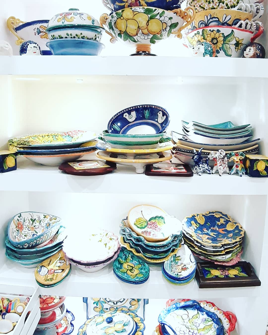 Scaffali pieni di piatti, ciotole e piatti da portata in ceramica colorata, di varie forme e fantasie.