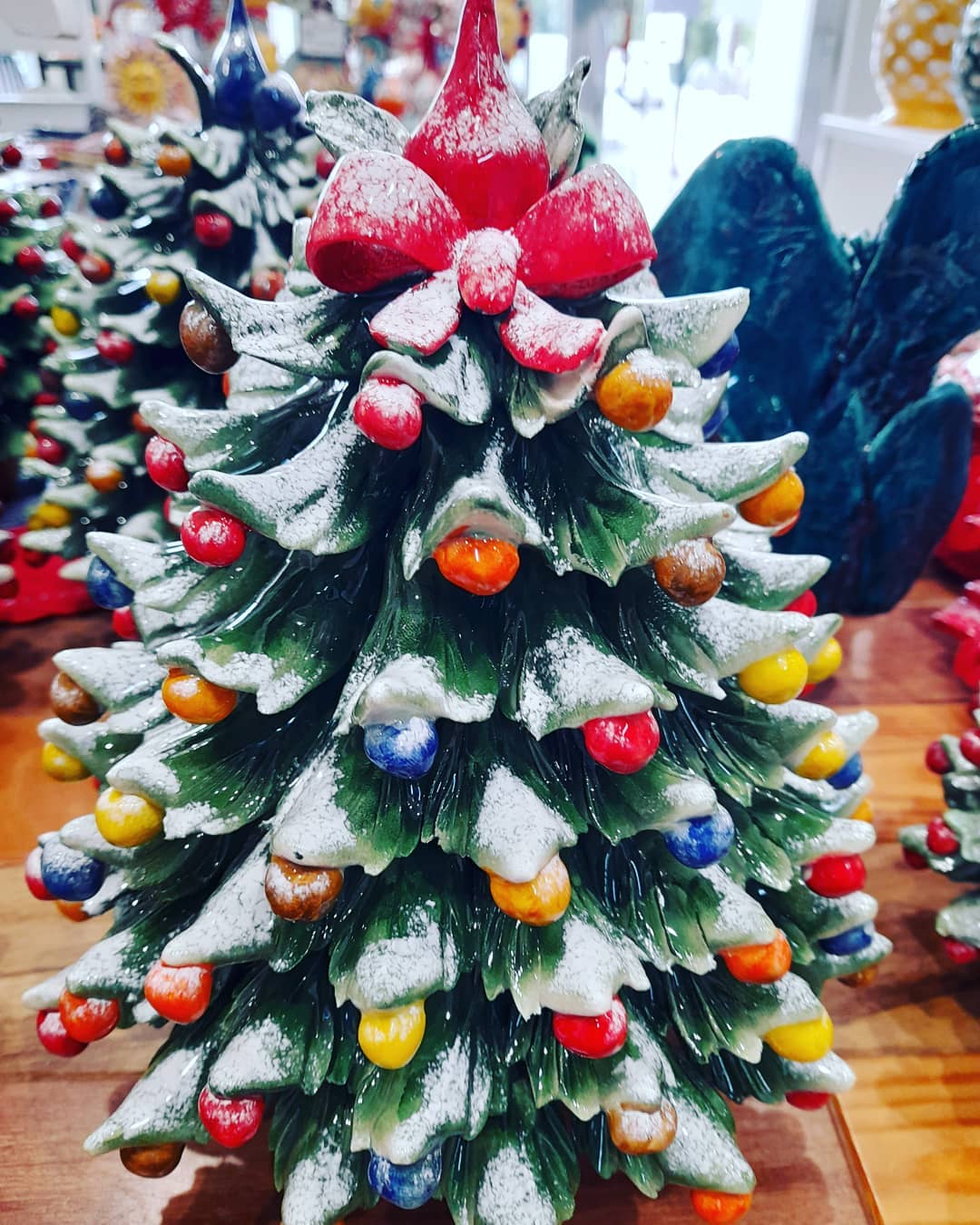 Albero di Natale in ceramica con fiocco rosso, decorazioni colorate e spolverata di neve.
