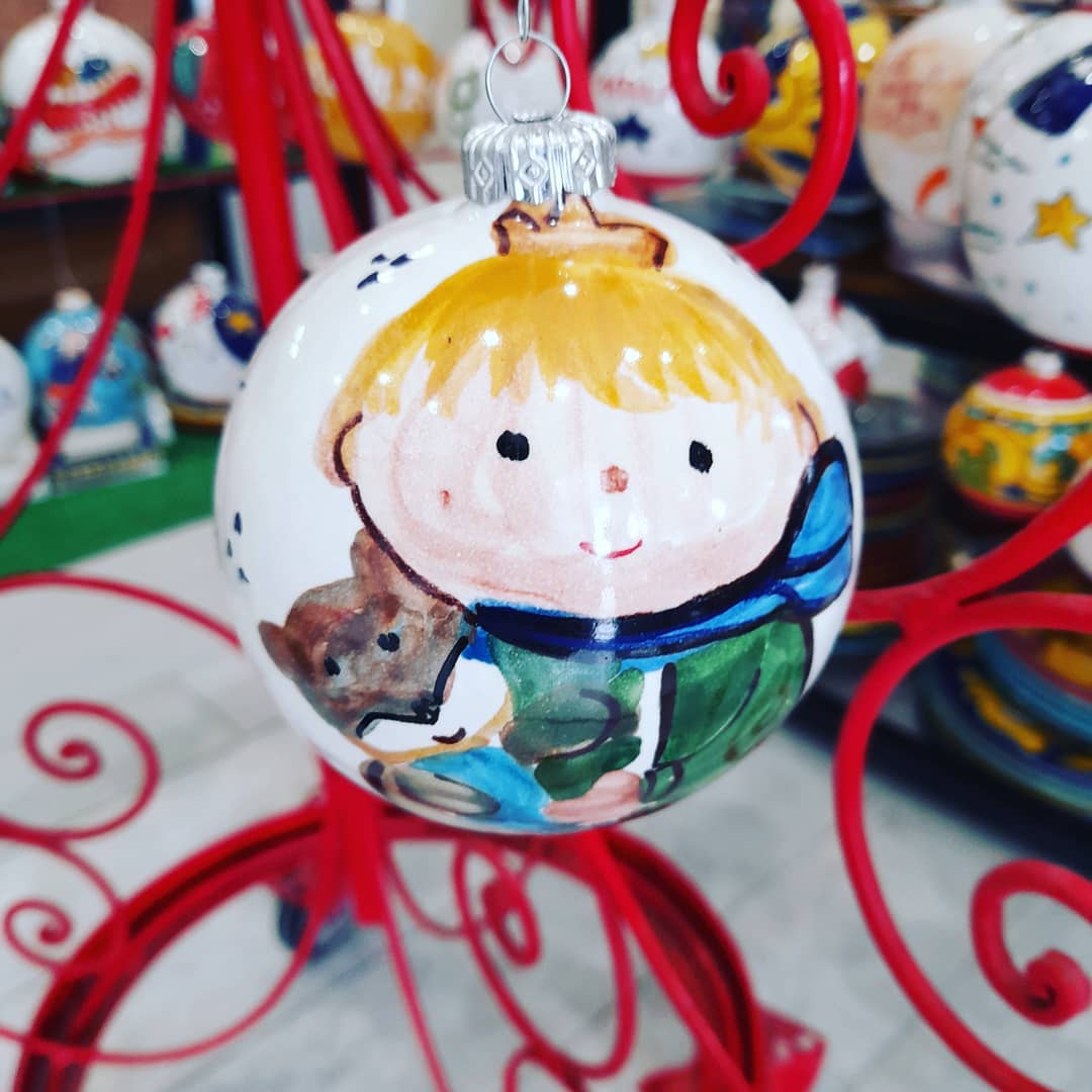 Decorazione natalizia dipinta a mano: un bambino biondo che abbraccia un cucciolo marrone. La decorazione è bianca con dettagli rossi e verdi.