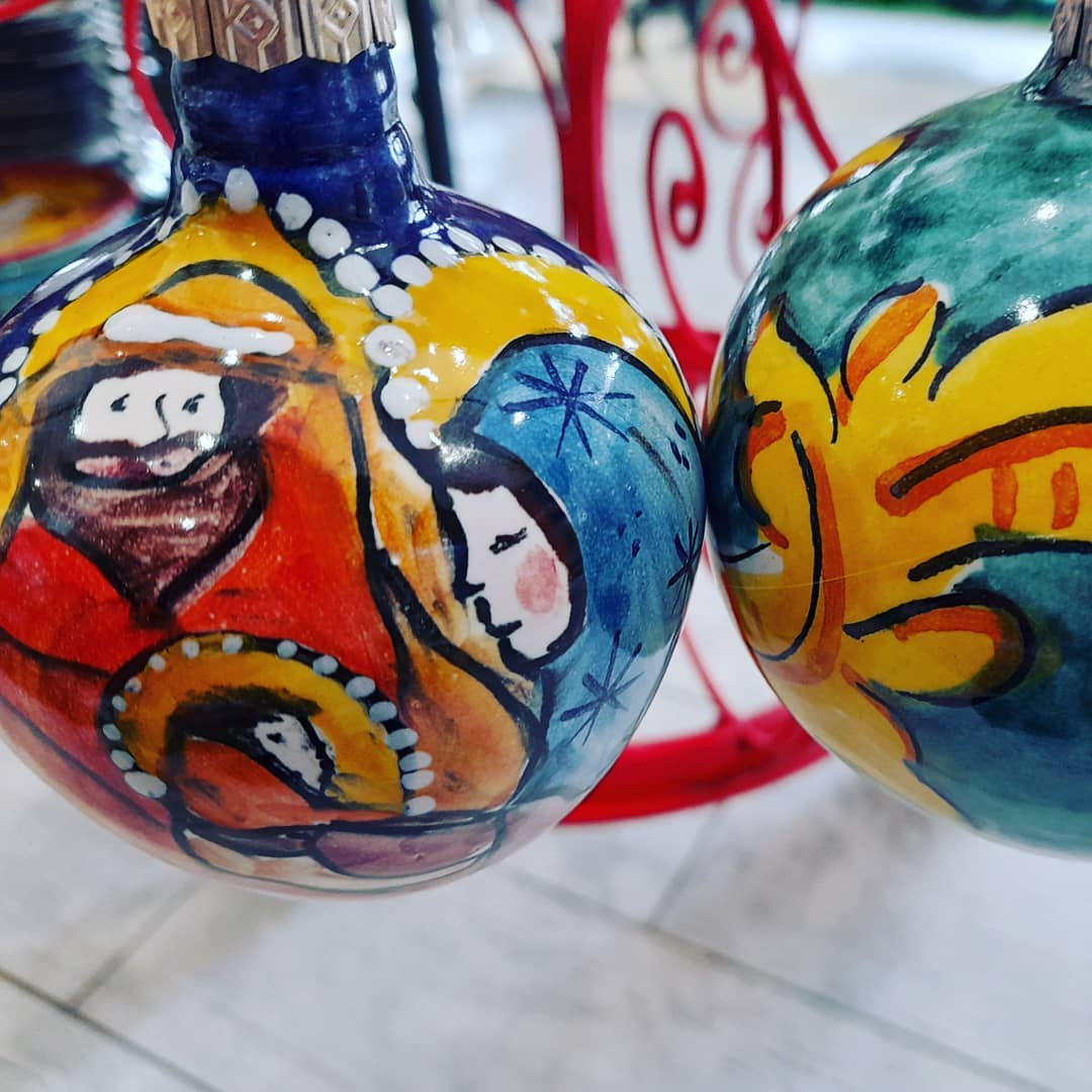 Due decorazioni natalizie dipinte a mano: presepe con figure colorate, dettagli gialli e arancioni.
