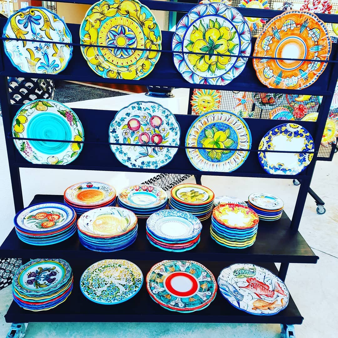 Esposizione di piatti di ceramica colorati e dipinti a mano su uno scaffale nero a più livelli, probabilmente in vendita.