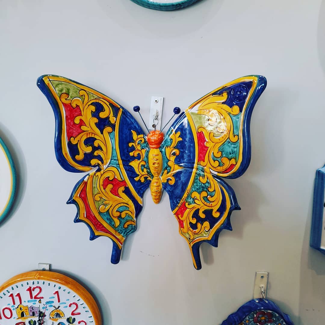 Decorazione da parete in ceramica a forma di farfalla, blu, gialla, rossa e verde.