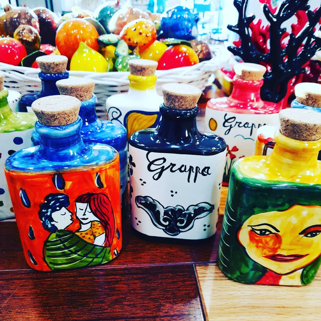 Bottiglie di ceramica colorate e dipinte con tappi di sughero; alcune riportano l'etichetta