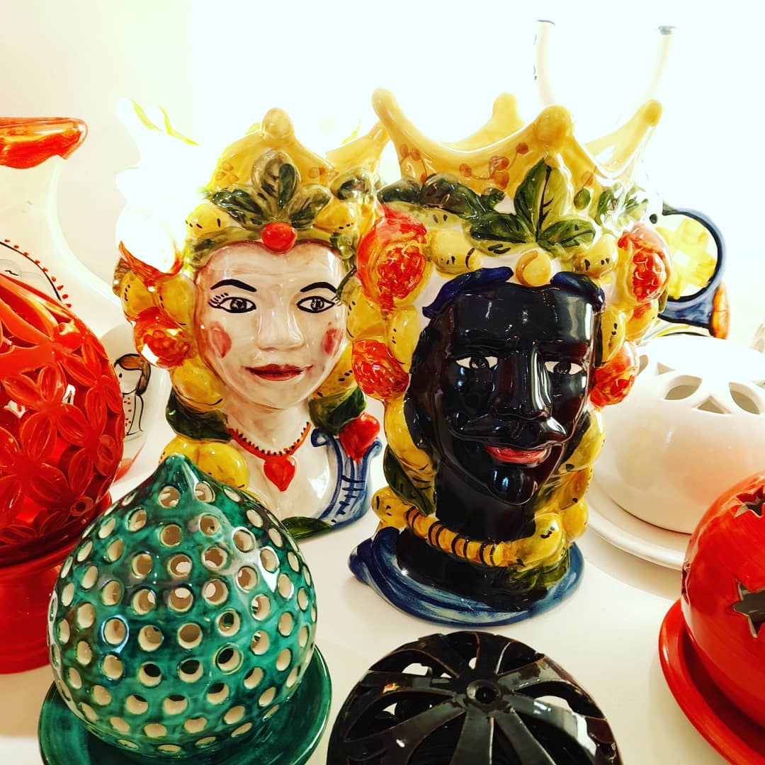 Teste di ceramica, una dalla pelle chiara, una nera, con corone, circondate da ceramiche colorate su una superficie bianca.