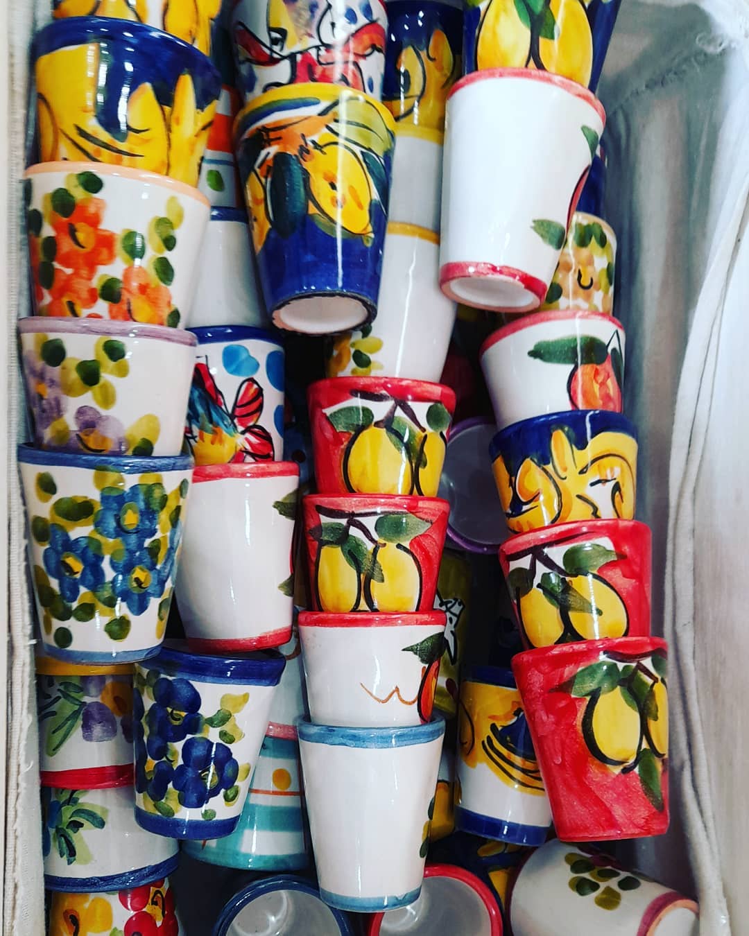 Tazze in ceramica dipinte a mano con vivaci motivi floreali e di frutta, in un cestino.