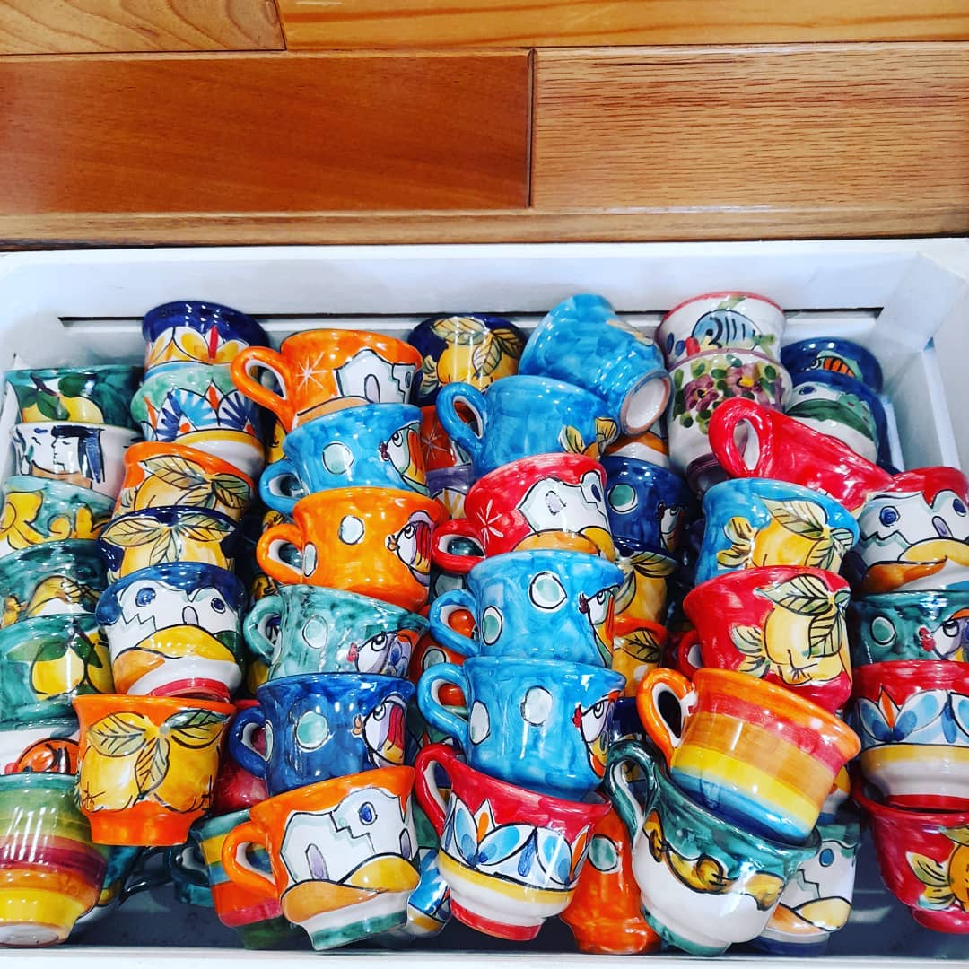 Tazze di ceramica colorate impilate su un vassoio, decorate con vari motivi dipinti e tonalità vivaci.
