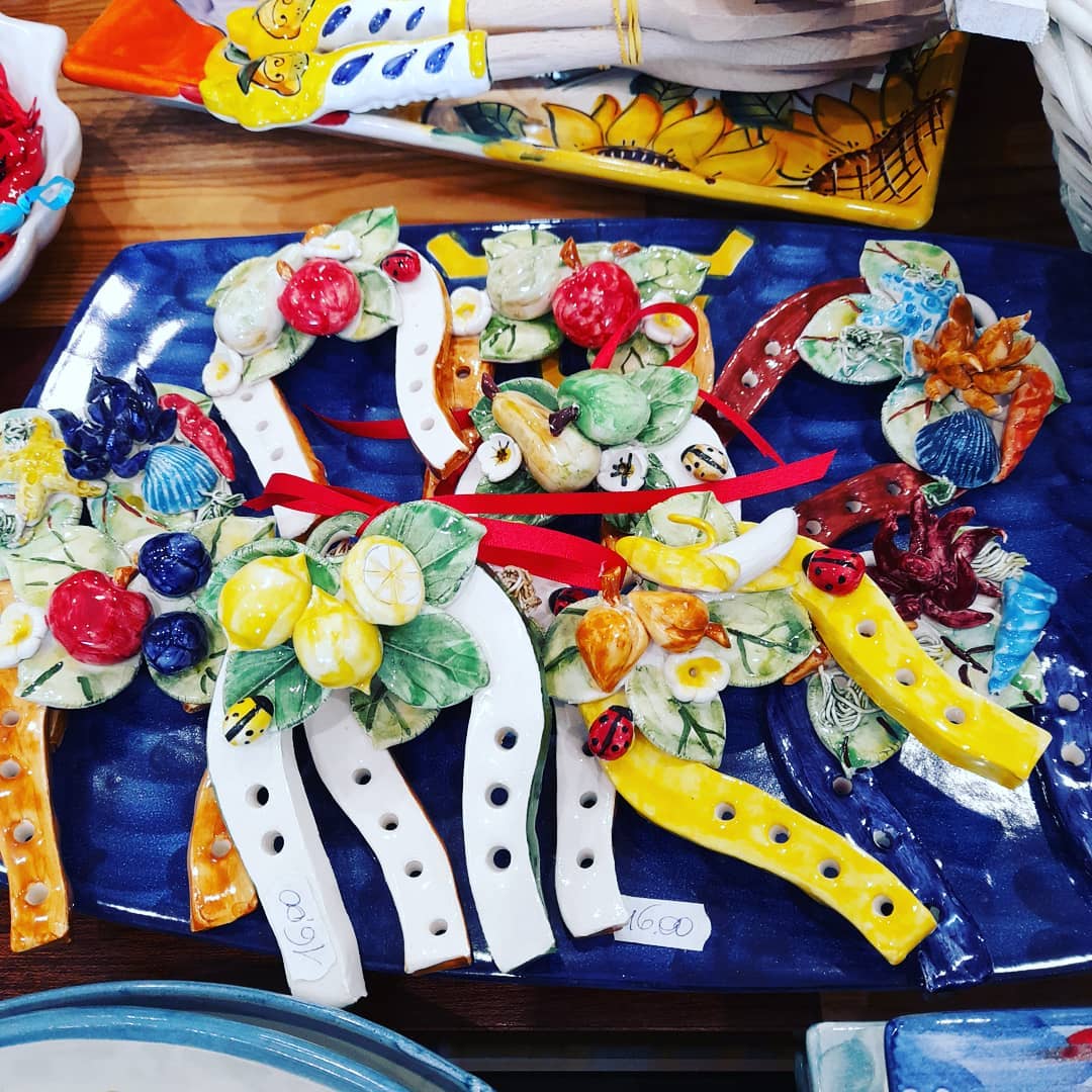 Decorazioni in ceramica a forma di ferro di cavallo con frutta, su un piatto blu, insieme ad altre ceramiche colorate.