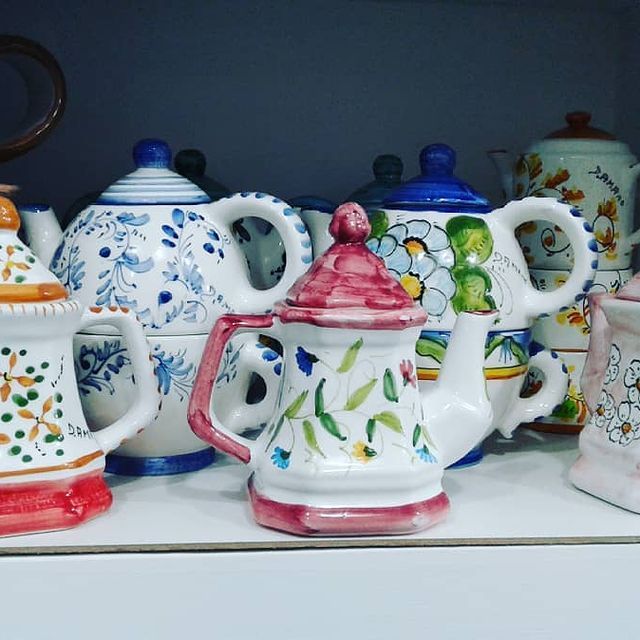 Assortimento di teiere in ceramica colorata su uno scaffale, ciascuna con un motivo dipinto unico.