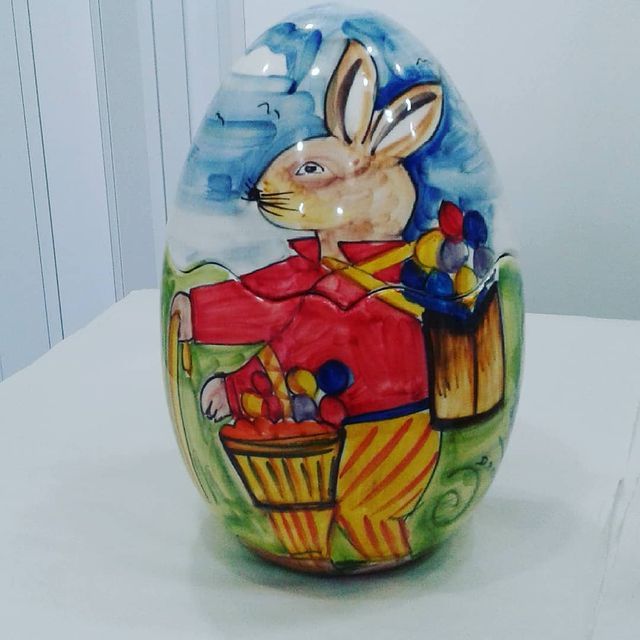 Uovo di Pasqua in ceramica raffigurante un coniglietto vestito con una giacca rossa e pantaloni a righe gialle.