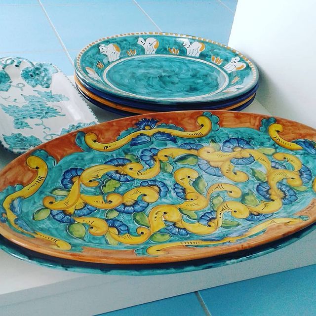 Piatti in ceramica dipinti a mano. Disegni vivaci blu, gialli e arancioni. Diversi impilati su uno scaffale.