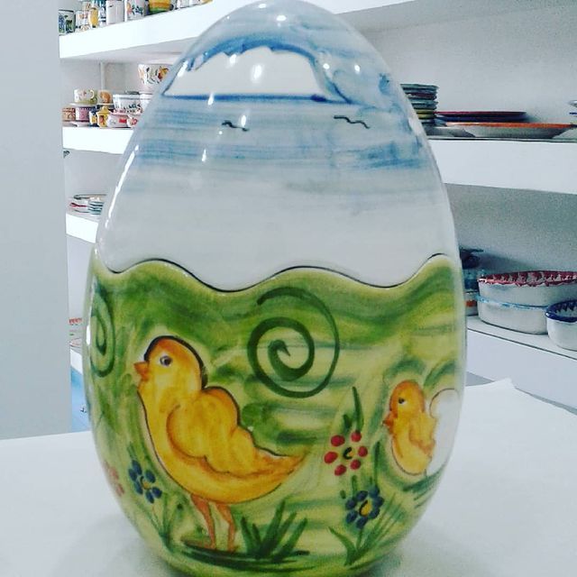 Grande uovo in ceramica decorato con una scena paesaggistica: pulcini nell'erba verde sotto un cielo azzurro.