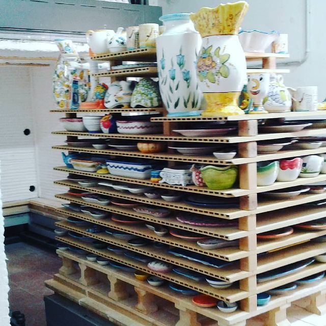 Ceramiche su scaffali impilati, una varietà di piatti dipinti, ciotole e vasi, in un ambiente da laboratorio.