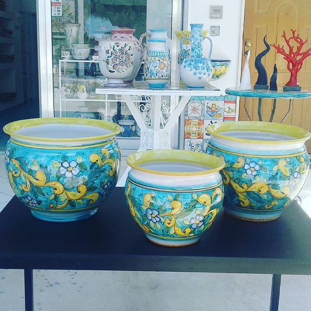 Tre vasi in ceramica turchese e gialla con motivi floreali sono appoggiati su una superficie nera, con altra ceramica sullo sfondo.