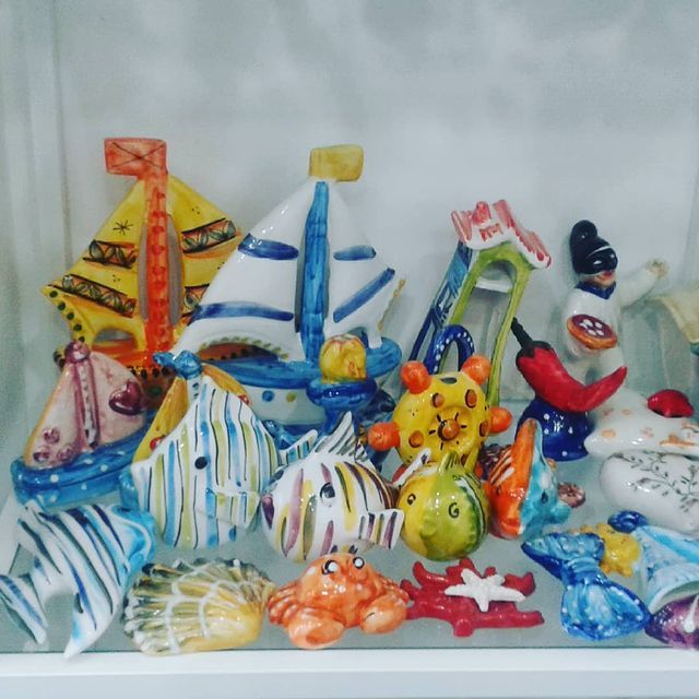 Statuine in ceramica colorate raffiguranti creature marine, barche e persone su uno scaffale.
