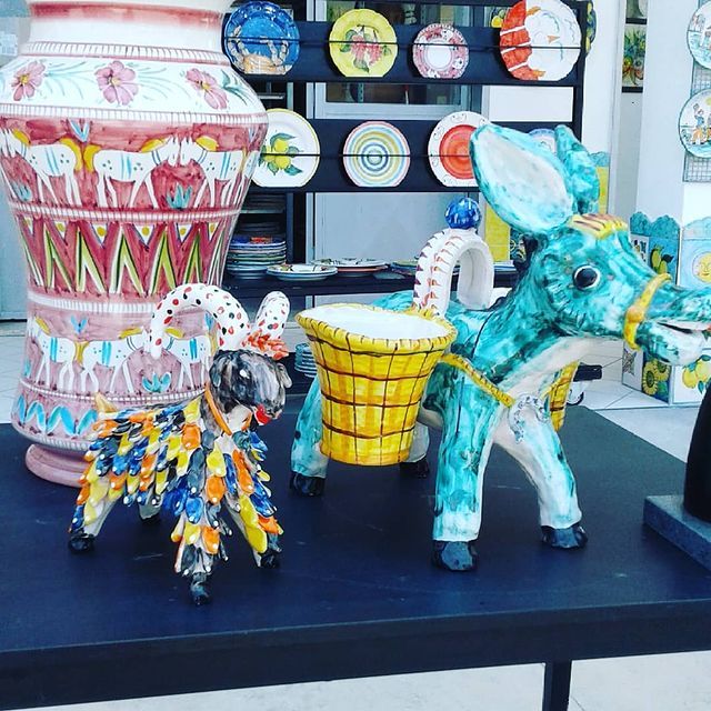 Due asini in ceramica con cesti e un grande vaso, esposti insieme a piatti in un negozio.