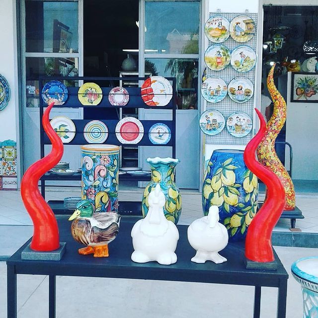 Esposizione di ceramiche artistiche colorate, tra cui piatti, vasi e sculture, con sculture curve rosse.