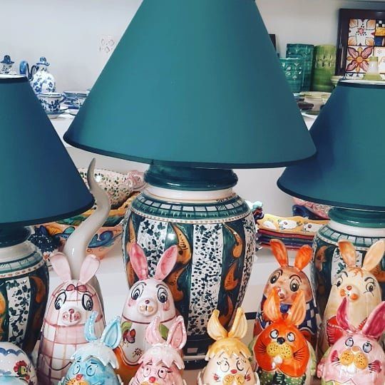 Su uno scaffale sono esposte statuette di coniglietti in ceramica e lampade decorative con paralumi color verde acqua.