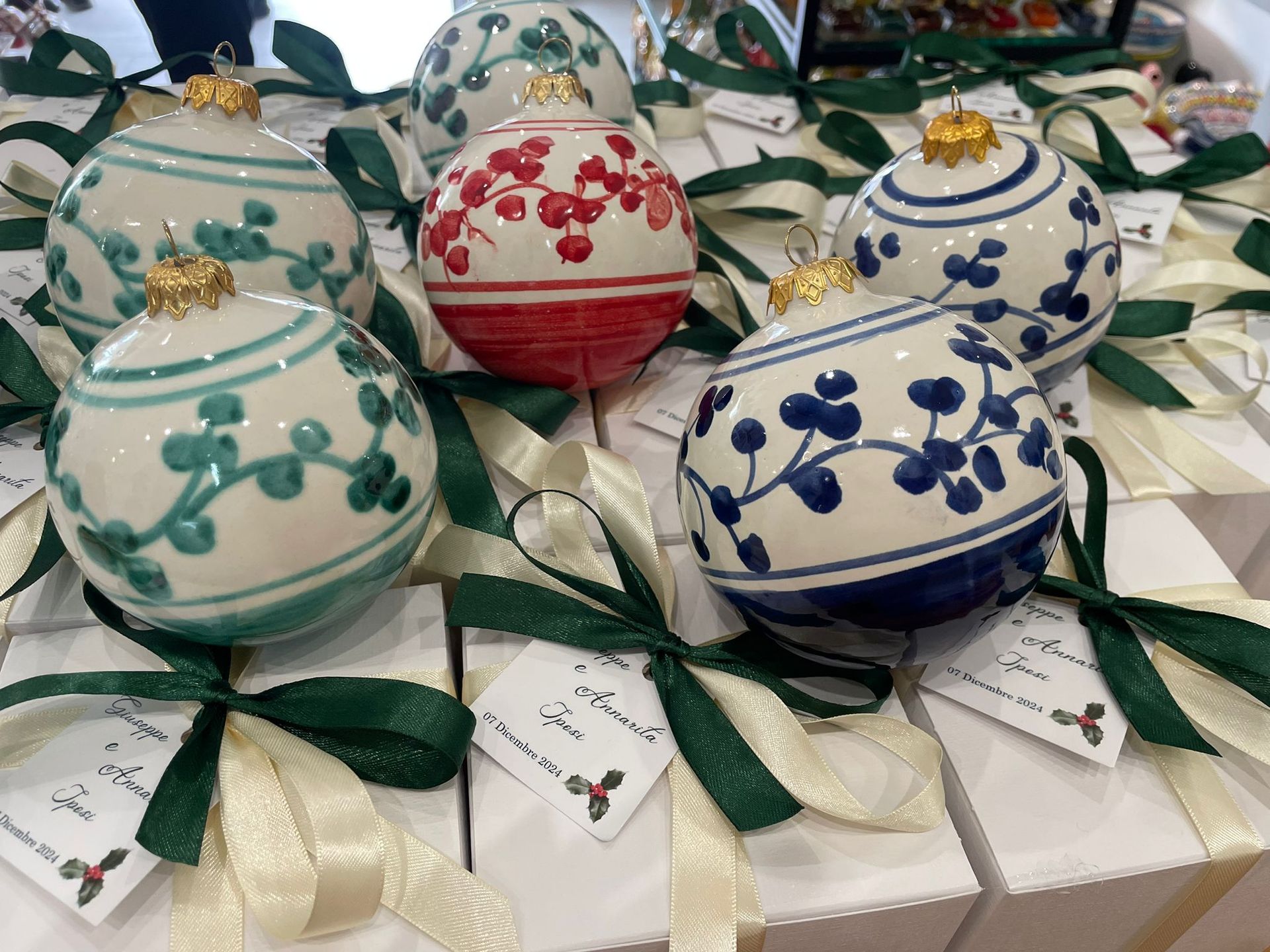 Decorazioni natalizie con motivi floreali dipinti su scatole regalo bianche legate con nastri verdi.