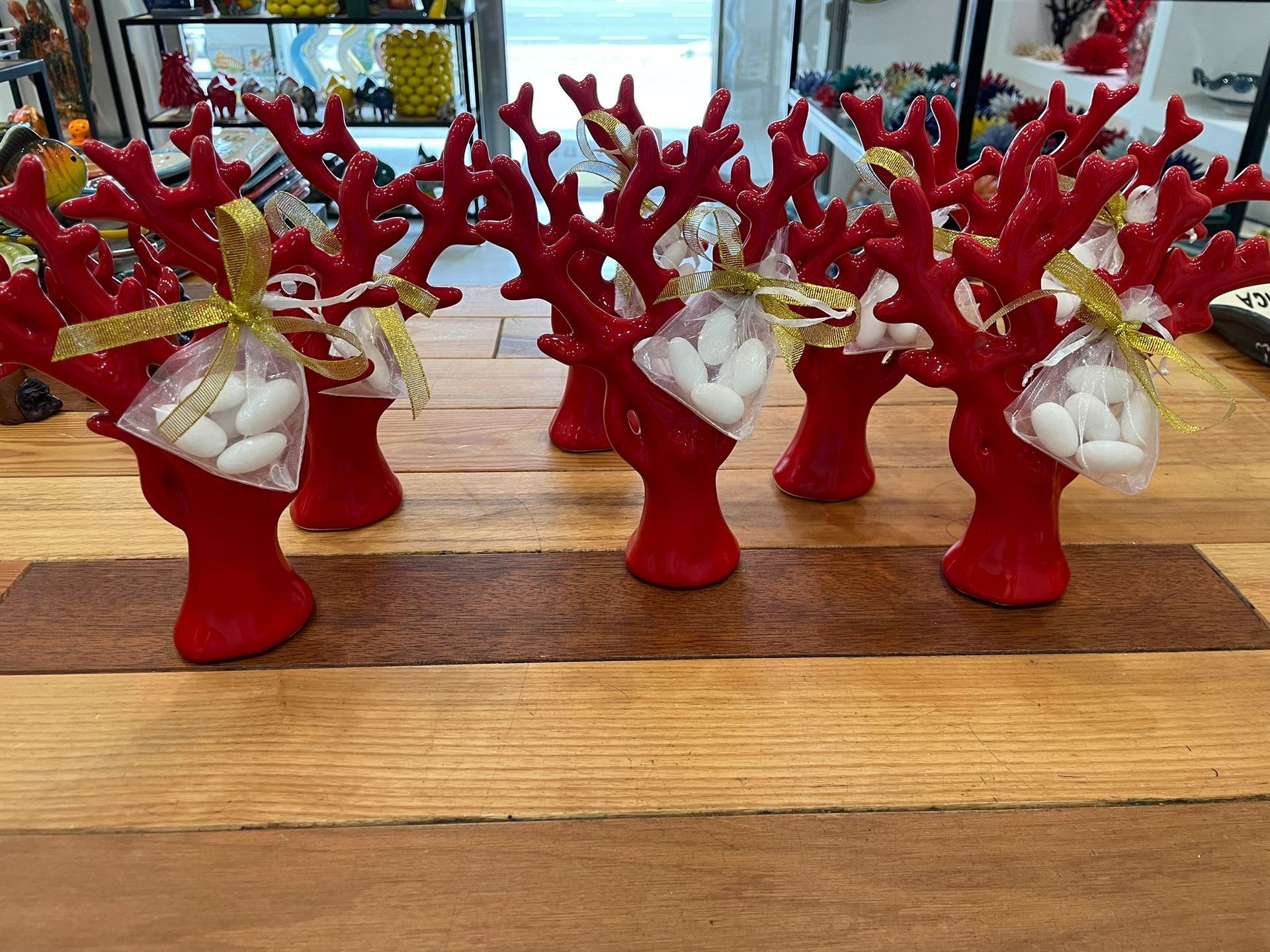 Su una superficie di legno sono appoggiate delle bomboniere a forma di corallo rosso, ciascuna con un sacchetto di caramelle bianche legato con un nastro dorato.