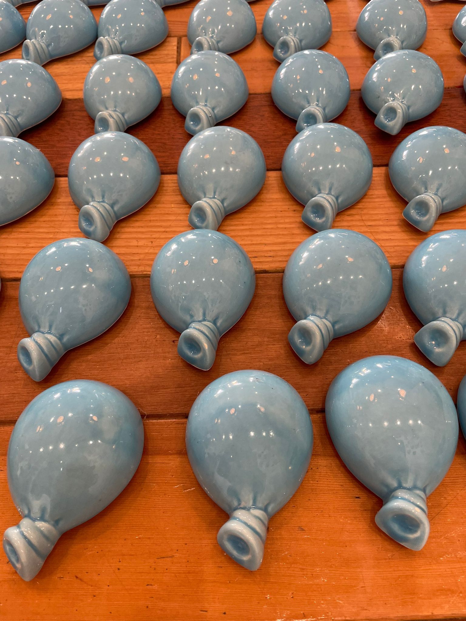 File di pezzi di ceramica blu lucida a forma di palloncino su una superficie di legno.