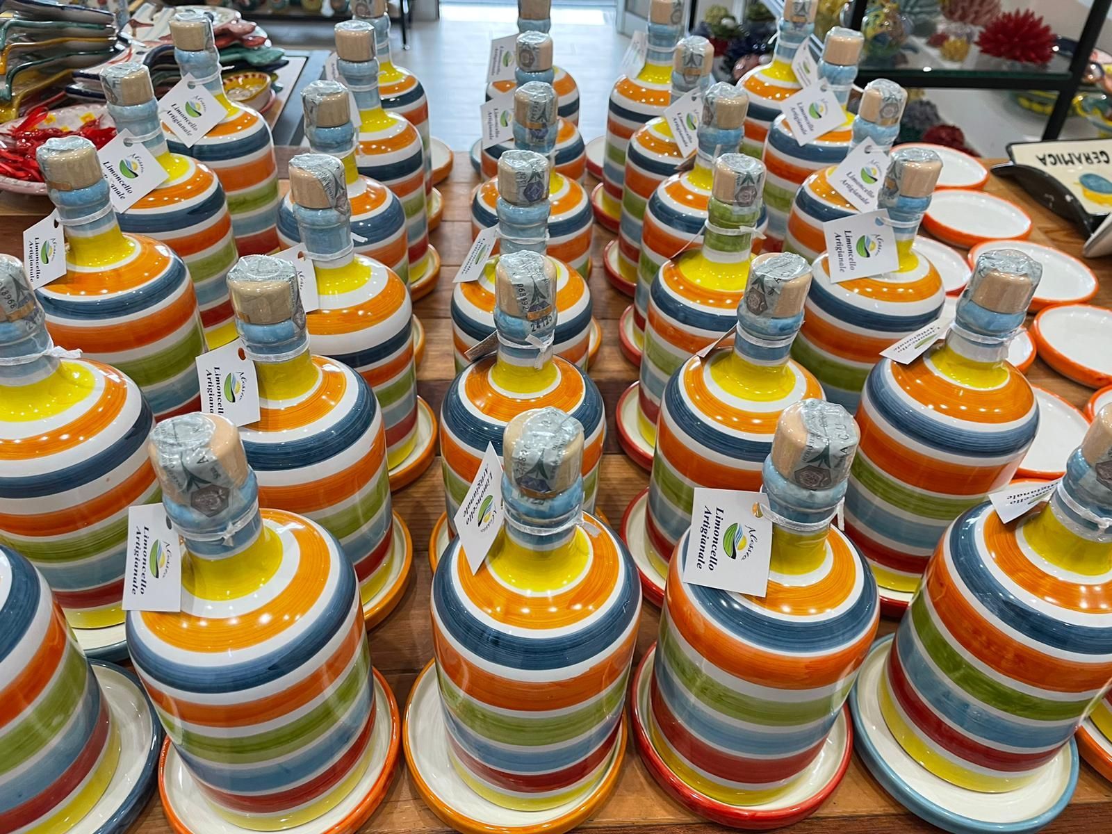 In mostra file di bottiglie di ceramica colorate a strisce, ciascuna con tappo di sughero ed etichetta.