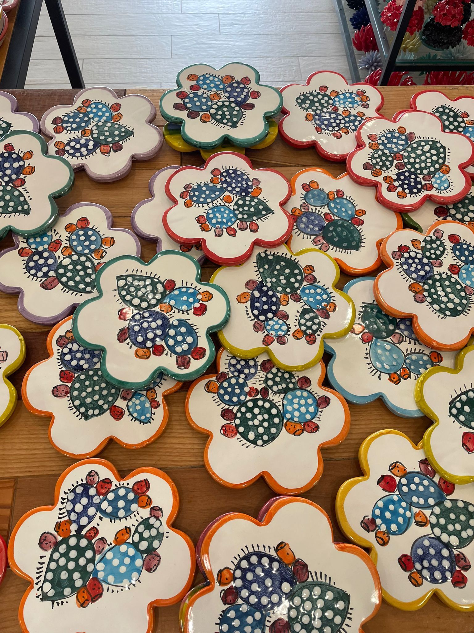 Sottobicchieri in ceramica a forma di fiore con motivi di cactus; bordi di vari colori: arancione, verde, blu, giallo e lavanda.