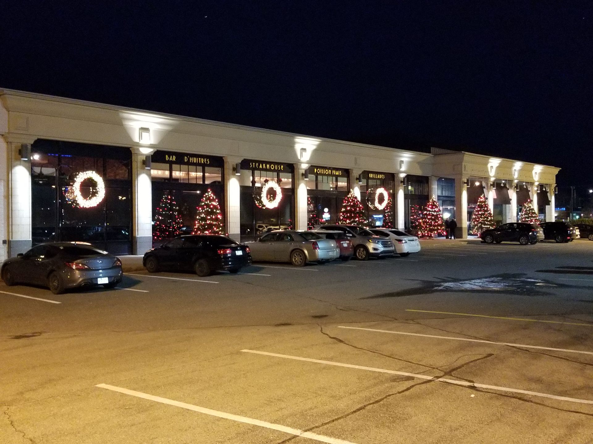 A row of cars are parked in front of a building decorated for christmas