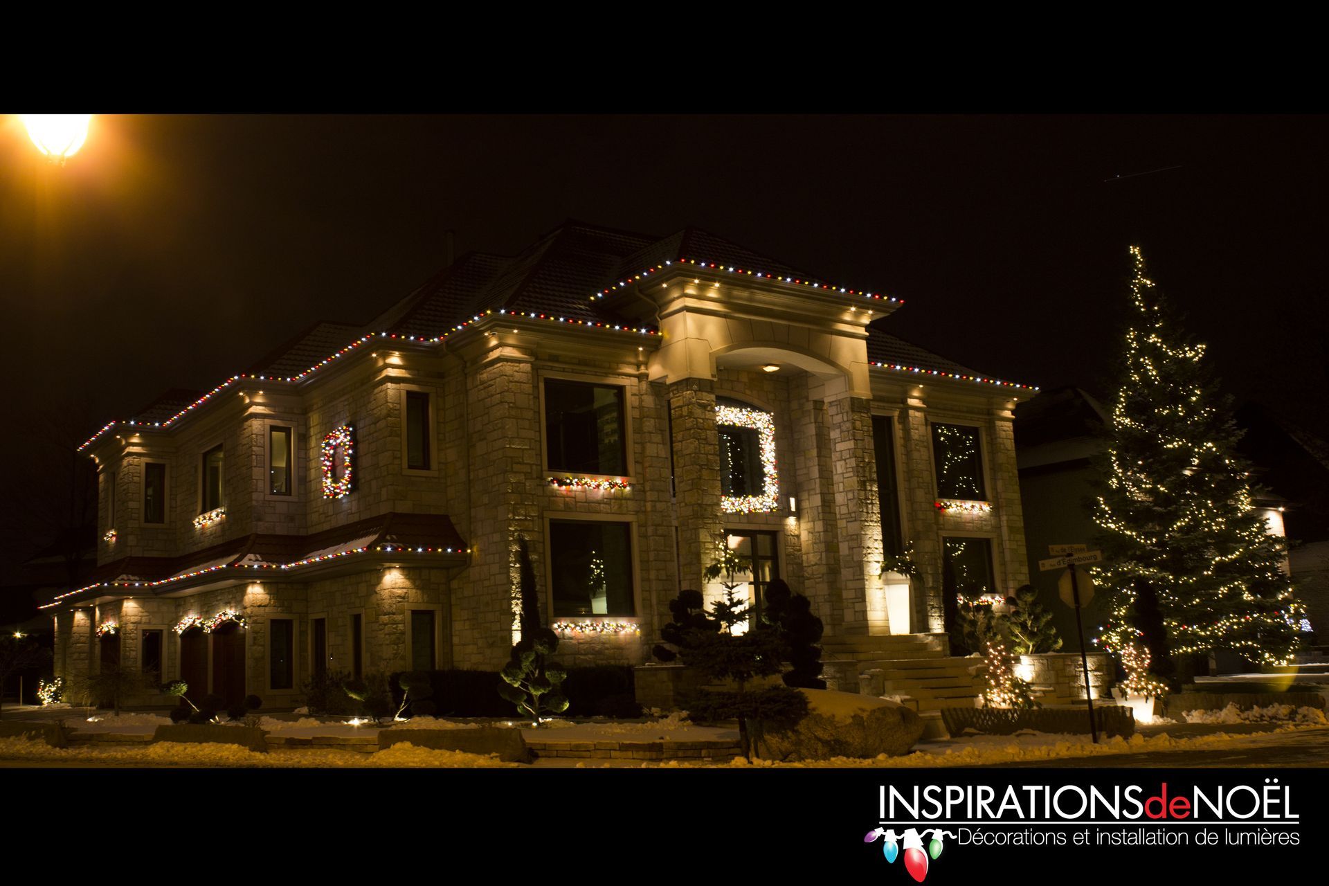 A large house is decorated with christmas lights and has a christmas tree in front of it