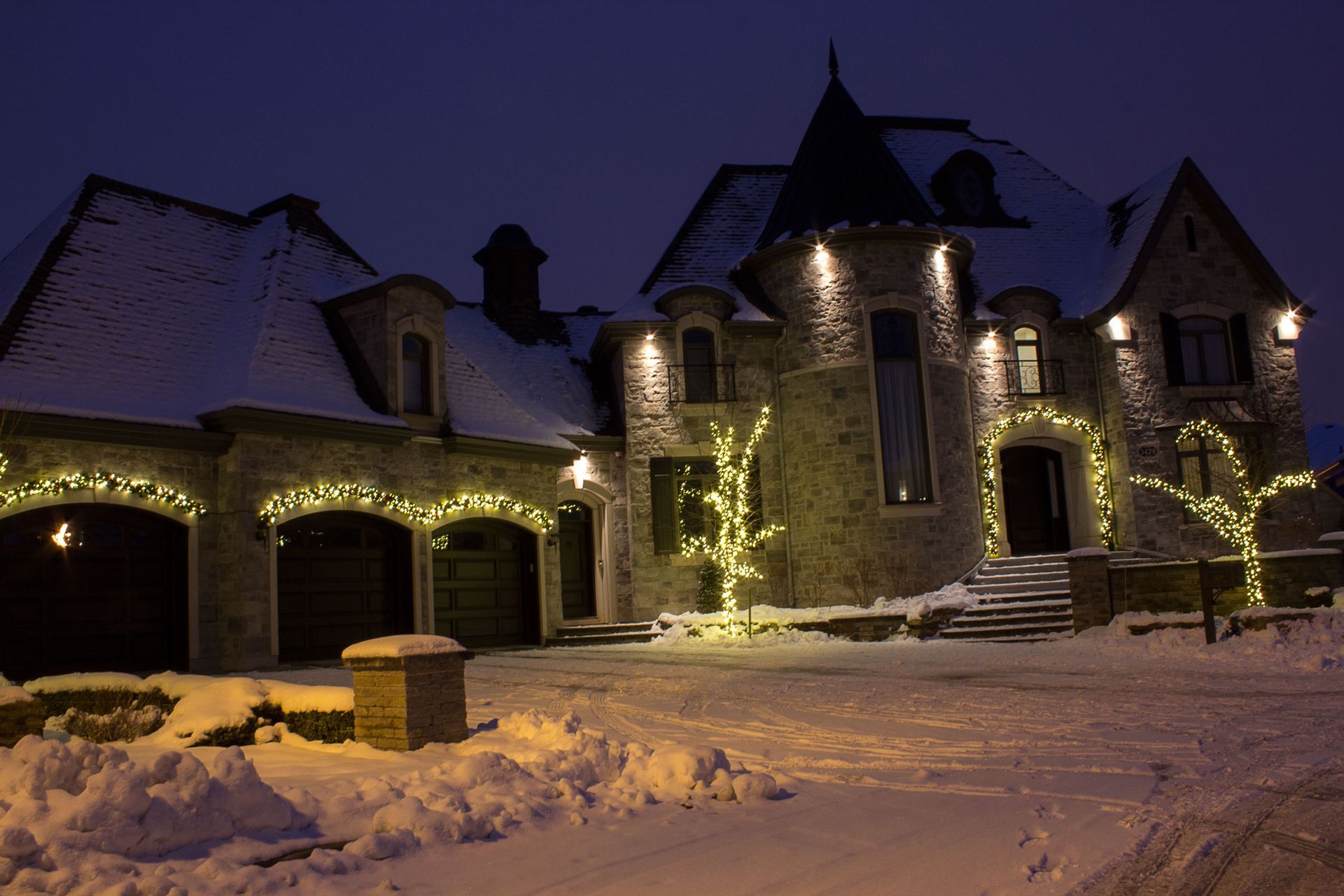 A large house with christmas lights on it is covered in snow.