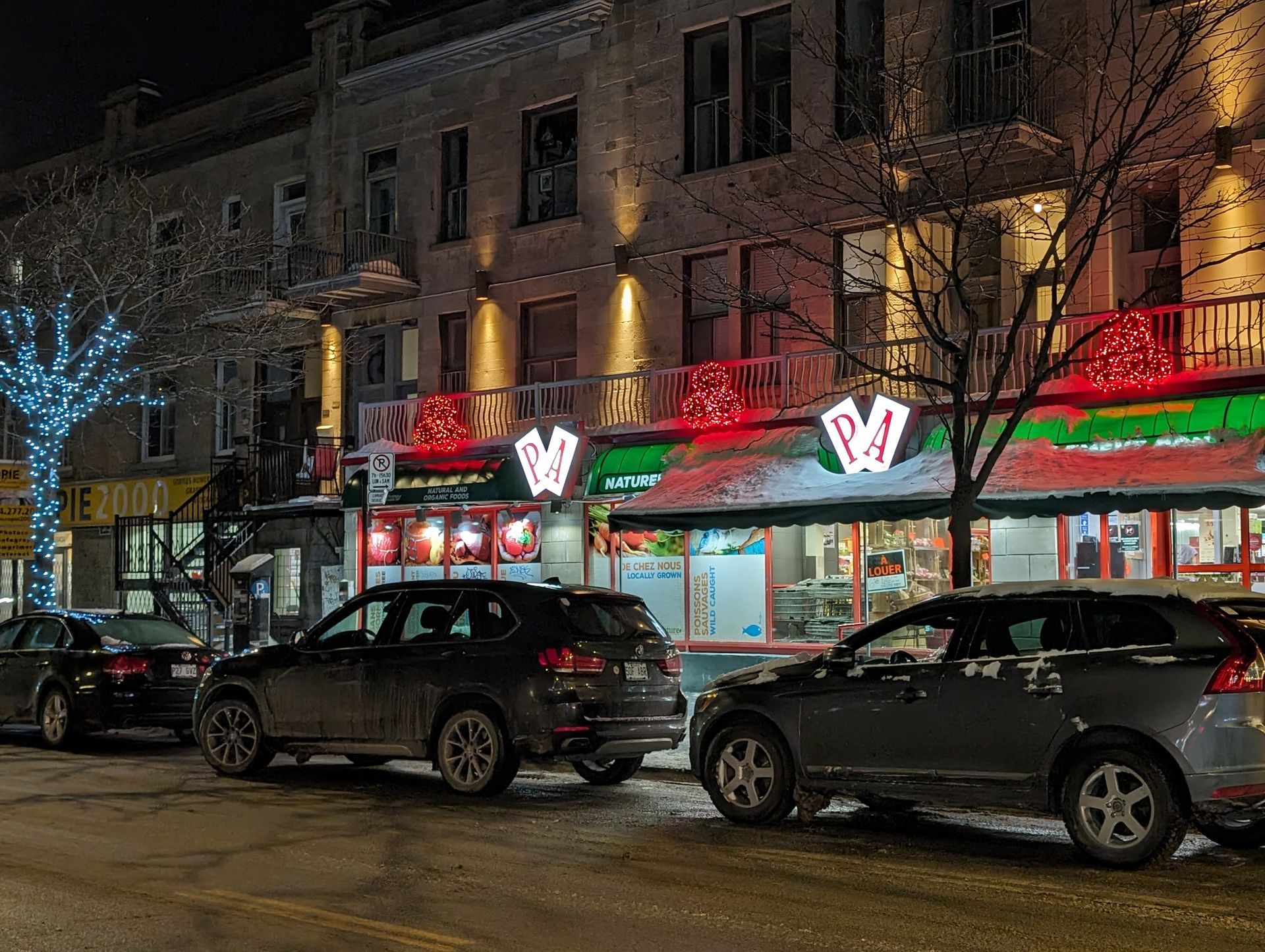 A row of cars are parked in front of a restaurant at night.