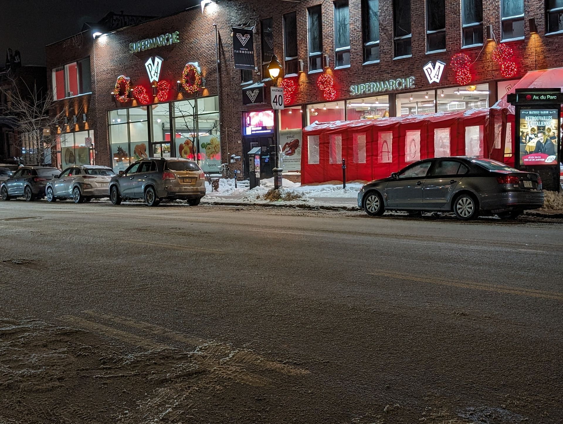 A row of cars are parked in front of a building at night.