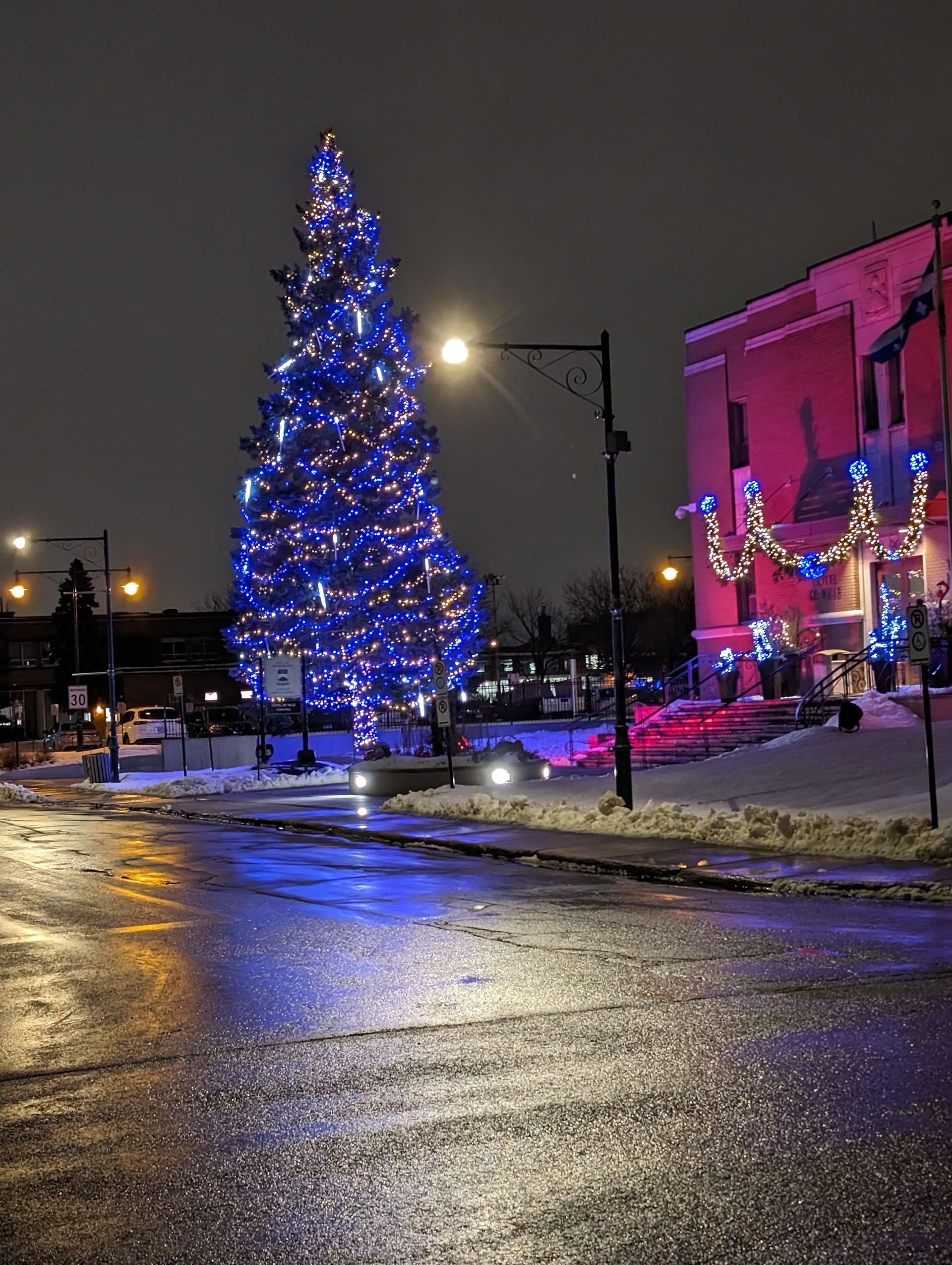 A christmas tree is lit up with blue lights in front of a building at night.