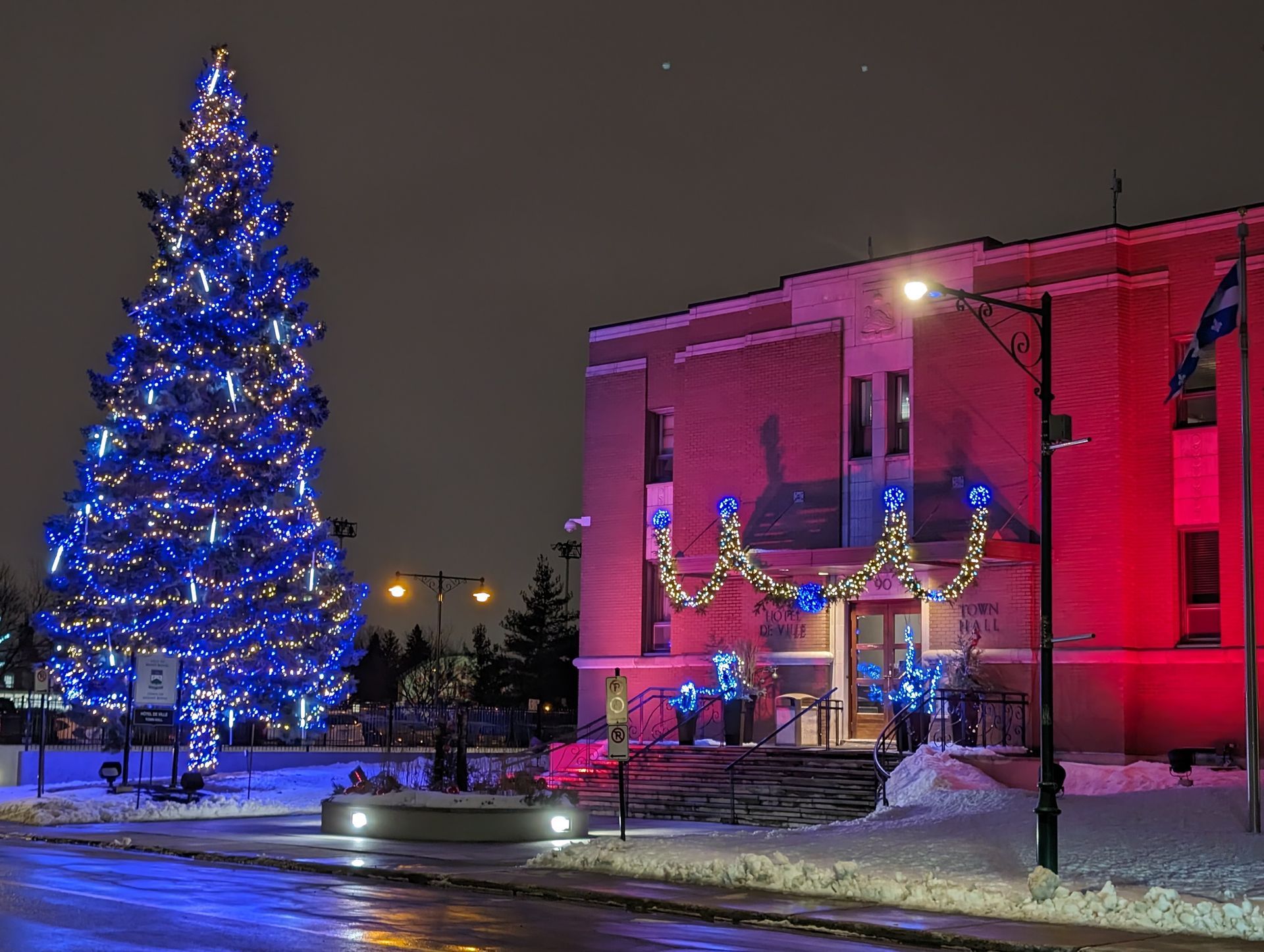 A christmas tree is lit up in front of a red building.