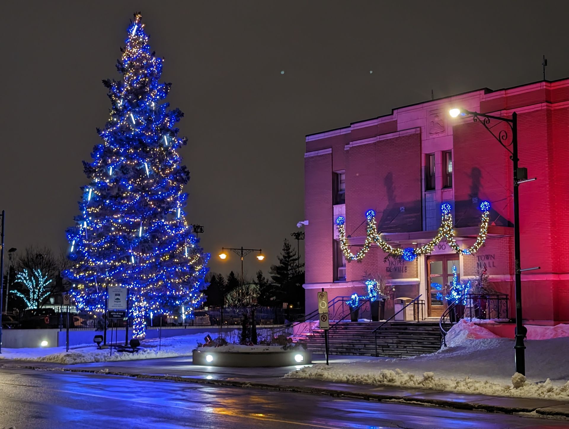 A christmas tree with blue lights is in front of a building at night.