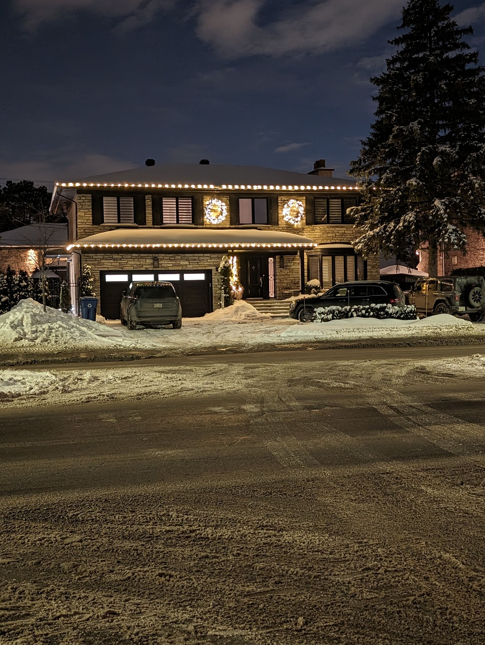 A house with christmas lights on it is covered in snow at night.