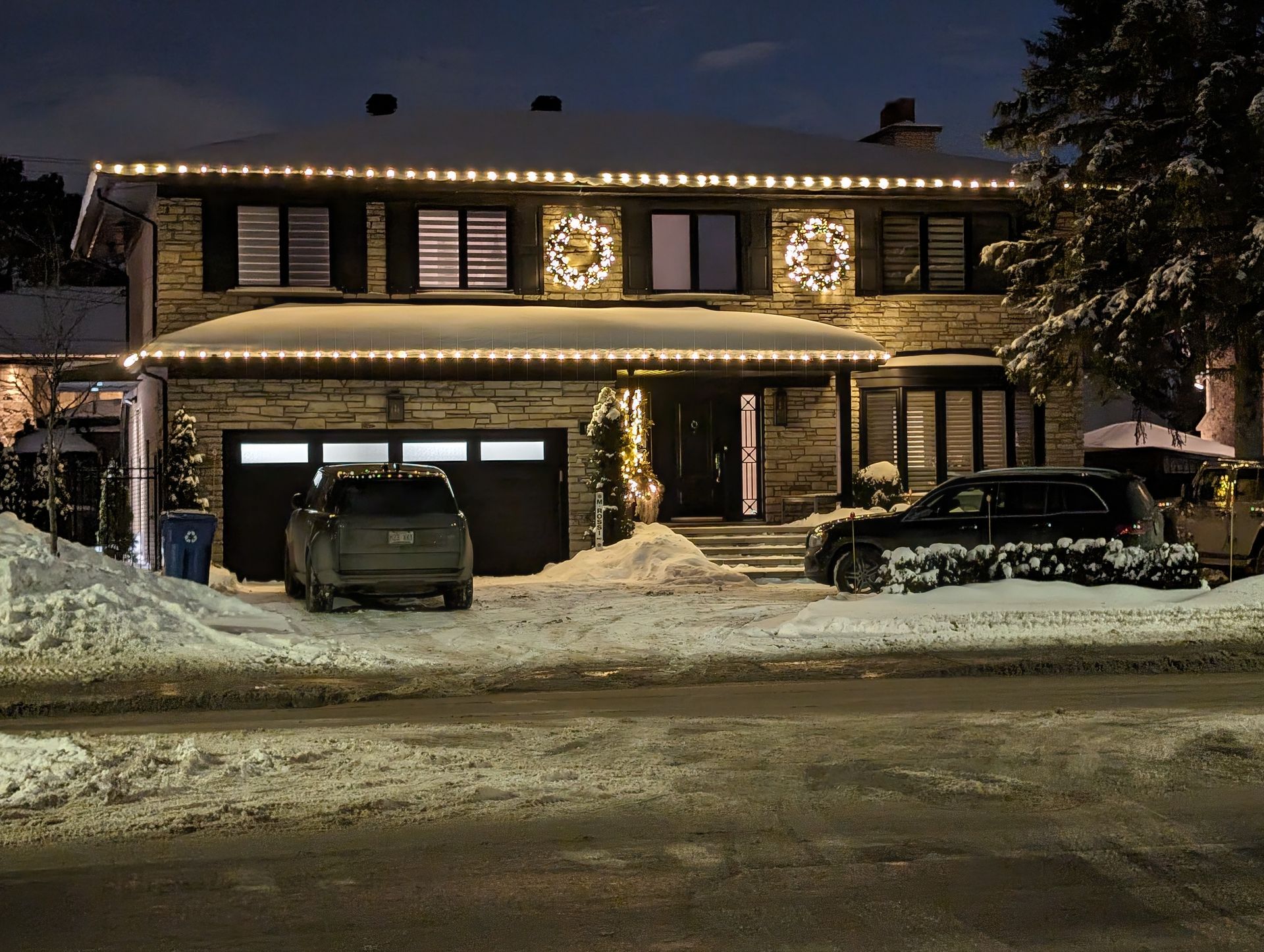 A house with christmas lights on it and cars parked in front of it