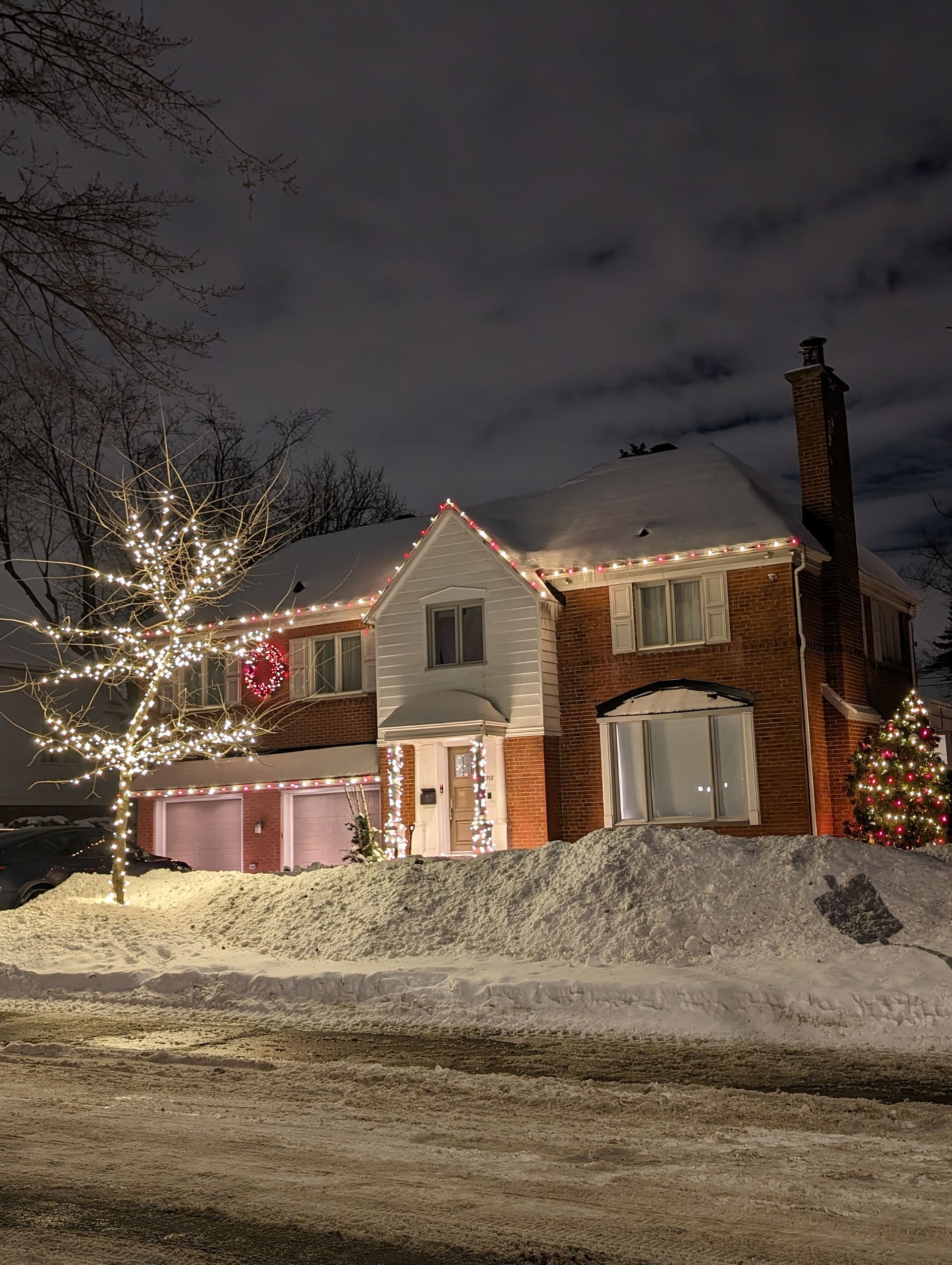 A house with christmas lights on it is covered in snow at night.