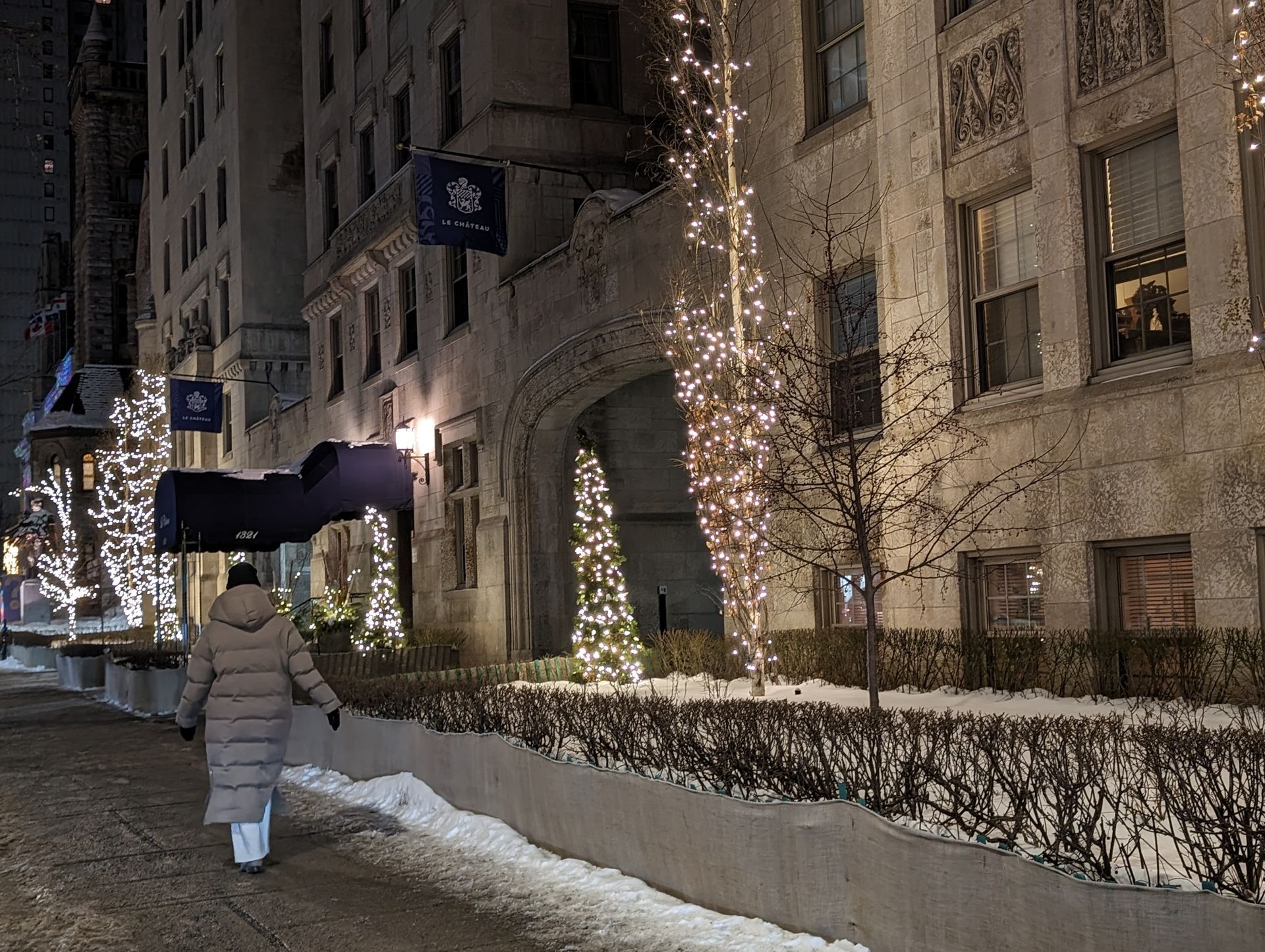 A person is walking down a snowy sidewalk in front of a building