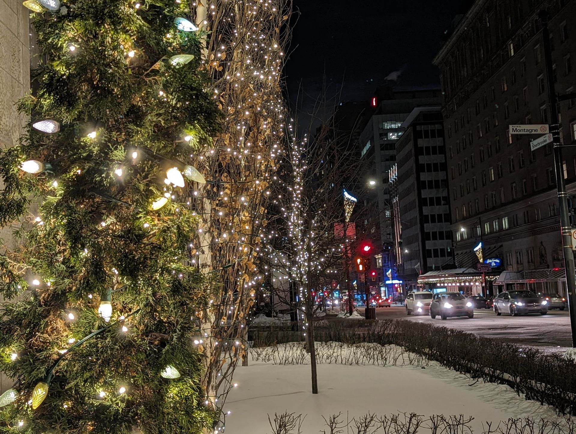 A christmas tree is lit up in front of a city street at night.