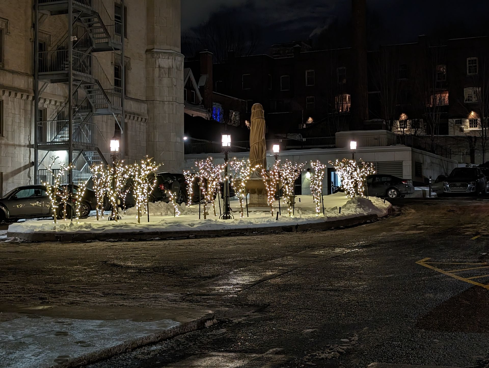 A statue is surrounded by christmas lights in a parking lot at night.